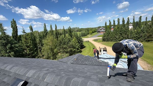 Person sealing roof shingles on a sunny day.