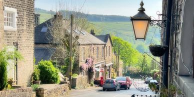 A view of Woods Lane, Dobcross with the village store and post office and church tower on the left.
