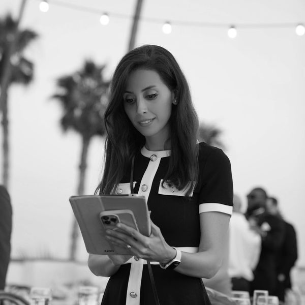 Woman in black dress using a tablet outdoors.