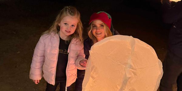 A woman and a girl holding a glowing lantern at night outdoors.
