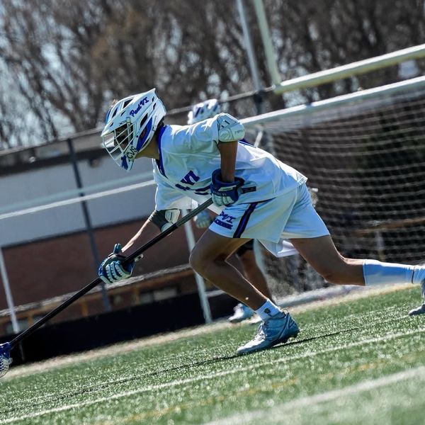 Lacrosse player in white gear lunging forward on the field during a game.