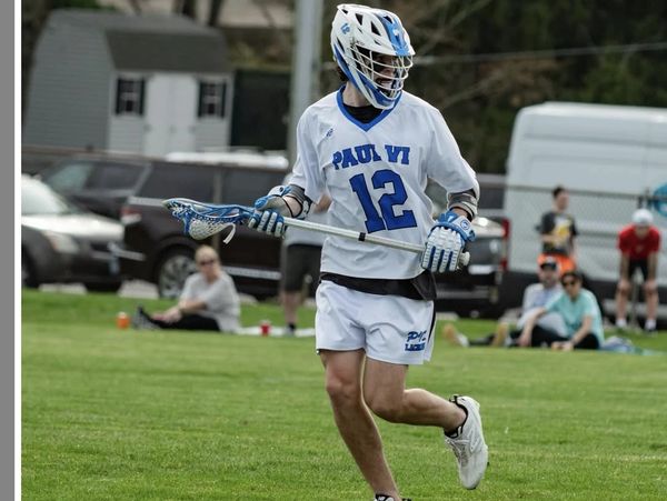 Lacrosse player in white and blue uniform running on field with stick.
