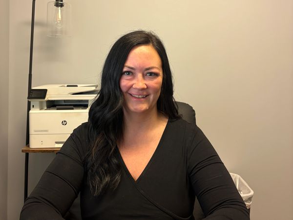 Smiling woman with long black hair sitting at a desk in an office.