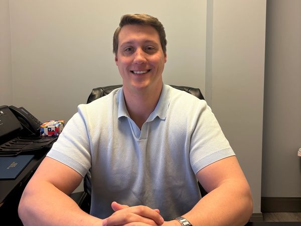 Man smiling while sitting at desk with hands clasped.