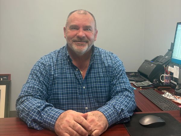 Smiling man in blue checkered shirt sitting at office desk.