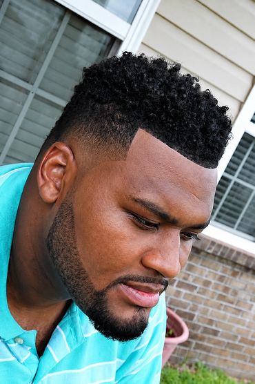 Man with a fresh curly high top fade haircut and a neatly trimmed beard.