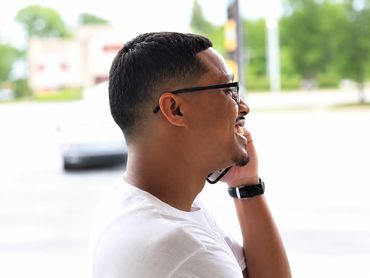 Man in white shirt smiling and talking on phone outdoors.