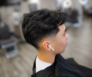 Man with a fresh fade haircut wearing wireless earbuds in a barbershop.