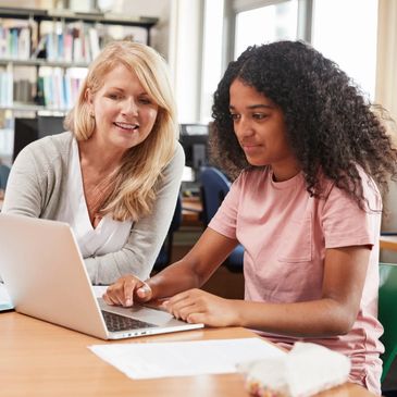 Speech therapy for teens. Adult woman and teen girl smiling and working together at a computer.