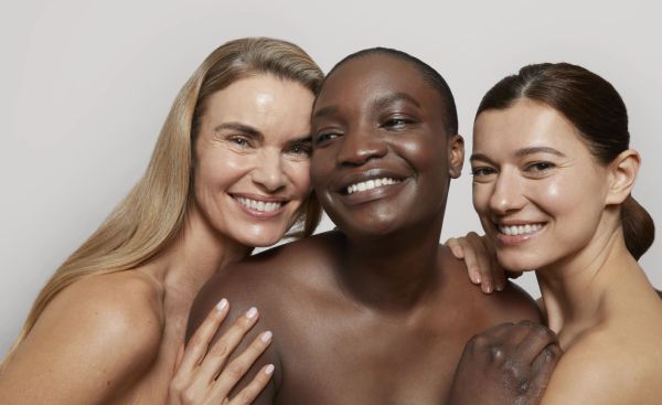 Three diverse women smiling and posing closely together.