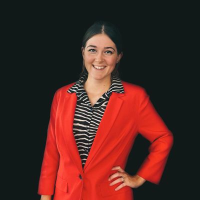 Smiling woman in a red blazer and zebra-striped shirt against black background.