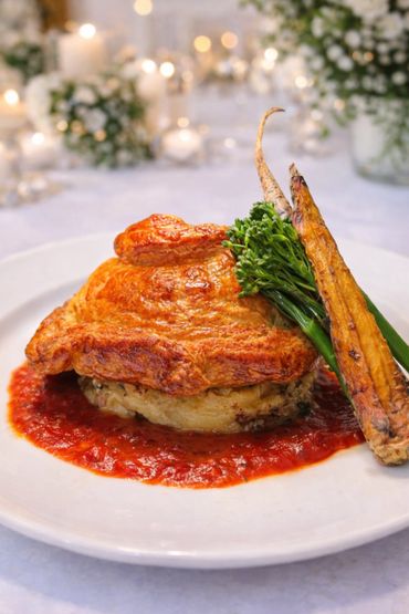Golden puff pastry with roasted vegetables and red sauce on a white plate.