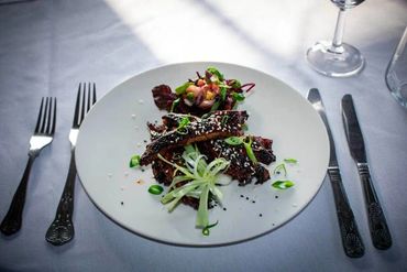 Grilled ribs garnished with green onions and sesame seeds on a white plate.