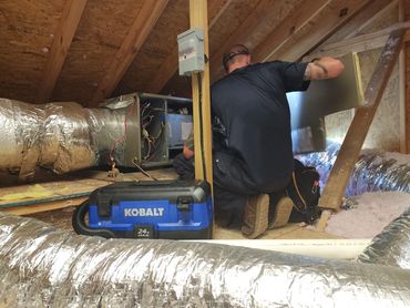 An HVAC technician kneeling in an attic while servicing an air handler unit.