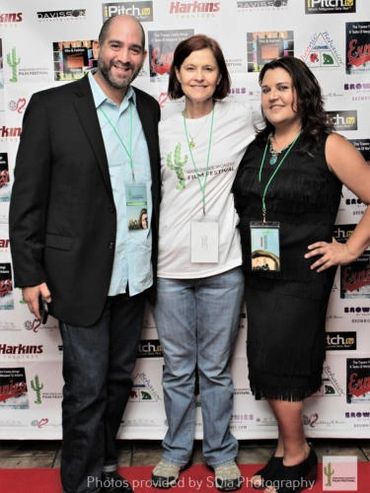 Kim Huenecke and Ava Louis with unidentified man in front of Step and Repeat