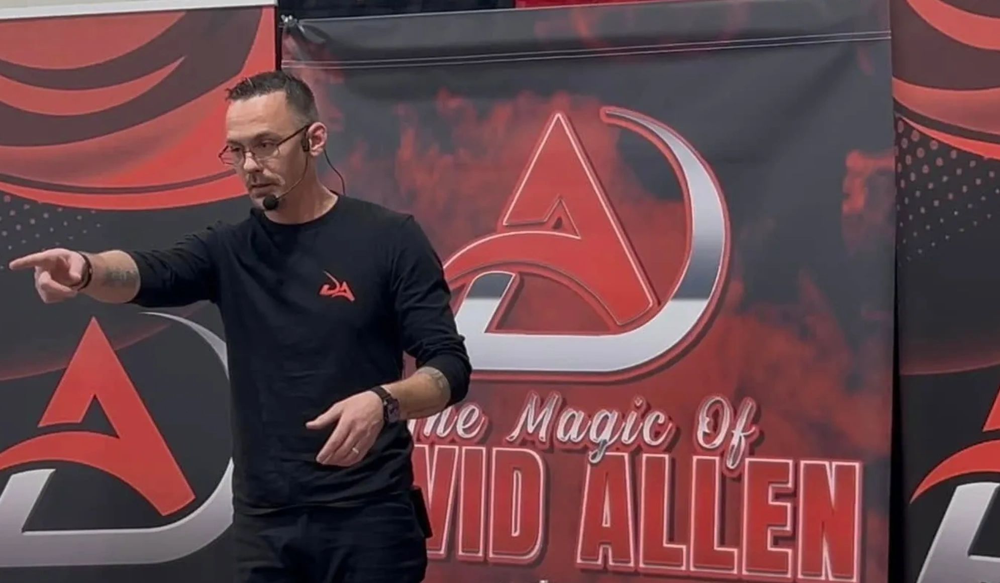 A man with a headset points while standing in front of a banner saying "The Magic of David Allen."