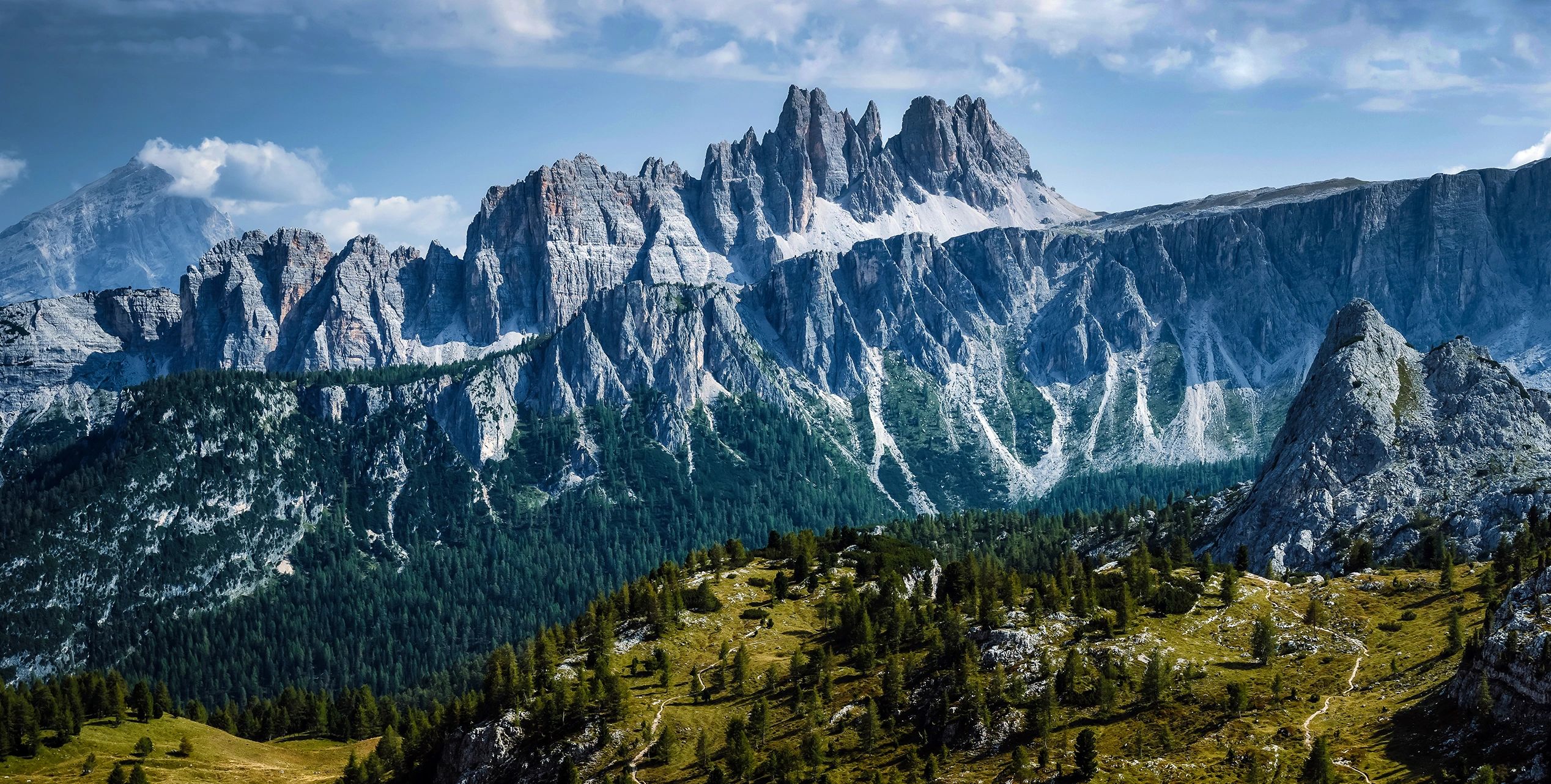 Stunning mountain range with rocky peaks and green forested slopes under a partly cloudy sky.