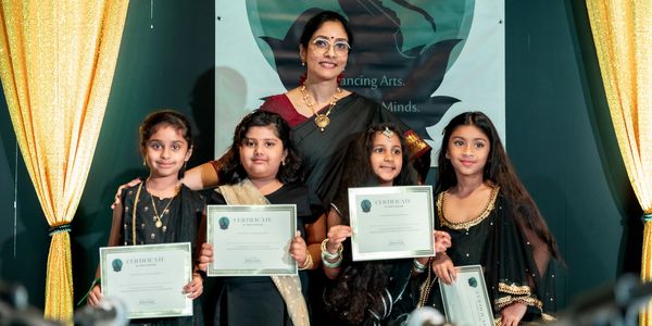 A woman with four girls holding certificates on a stage with golden curtains.