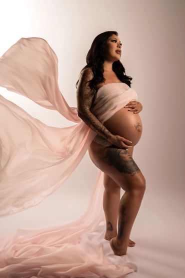 Pregnant woman draped in flowing pink fabric, showcasing her tattoos.
