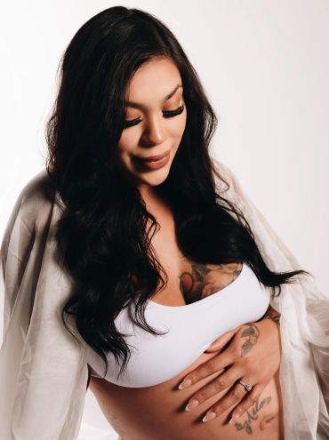 Pregnant woman lovingly holding her belly, wearing a white top and sheer cover-up.