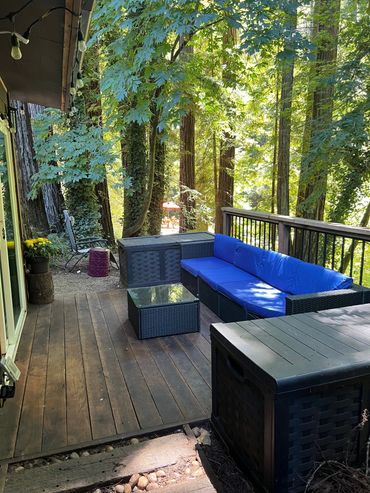A cozy outdoor deck with blue cushioned seating surrounded by tall trees and greenery.