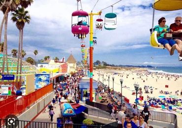 A crowded beachside amusement park with people and colorful sky rides.