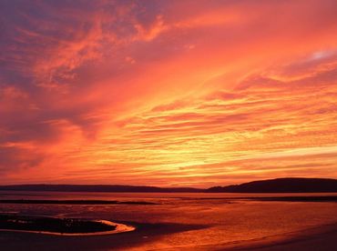 Vibrant orange and purple sunset over a calm beach landscape.