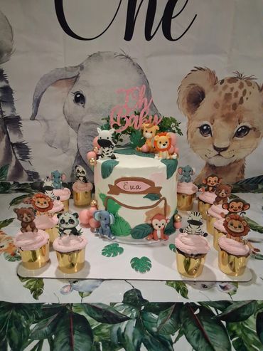 A jungle-themed birthday cake with animal cupcakes on a safari backdrop.