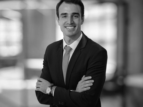 Confident young man in a suit with arms crossed, smiling professionally.