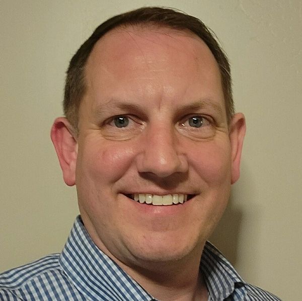 Smiling man in blue checkered shirt.