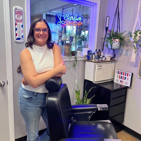 Woman standing in a barber shop next to a chair.