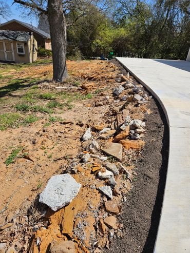 A garden bed lined with rocks and soil beside a concrete driveway.