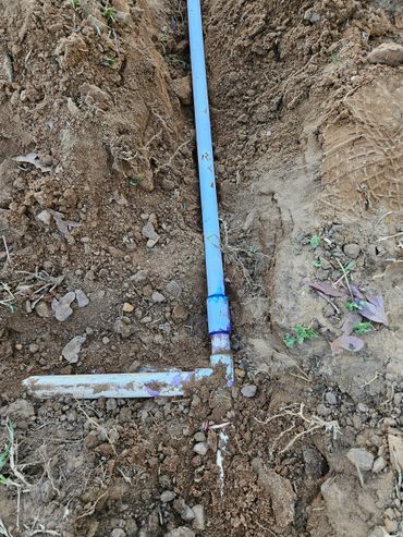 Blue PVC pipes connected underground in a dirt trench.