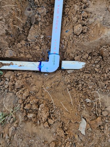 Broken white PVC pipe with elbow joint in dirt.