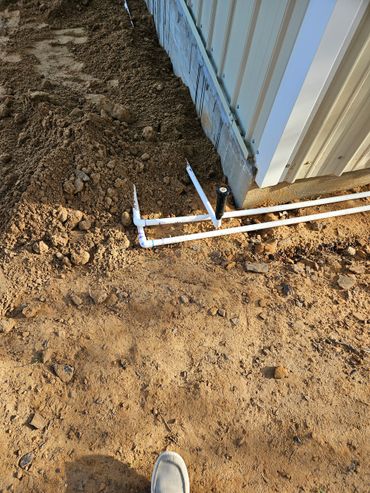 White PVC pipes near a metal building foundation with disturbed soil.