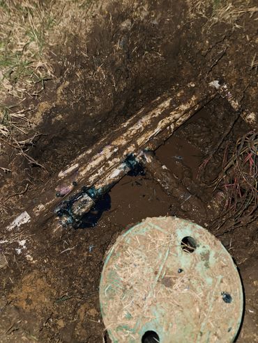 Exposed muddy pipes and cables in a dug-out ground area.