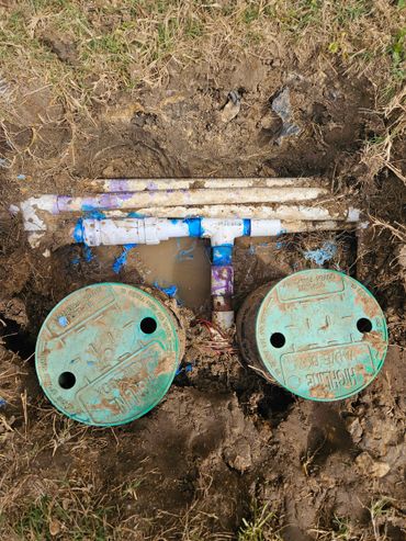 Two green valve boxes with exposed plumbing and blue markings in muddy ground.