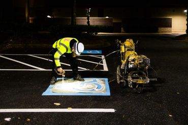 Worker painting a handicap parking symbol at night with a sprayer.