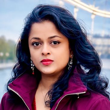 A woman with long dark hair wearing a maroon jacket and earrings.