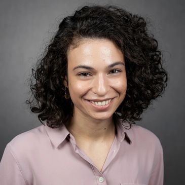 A young woman with curly hair smiling at the camera.