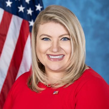 Smiling woman in red dress with American flag background.