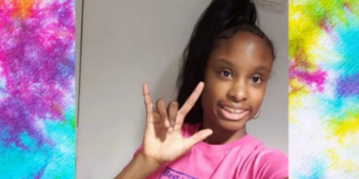 Young Black woman wearing a pink shirt, signing "I love you" Tye dye border on both sides of her