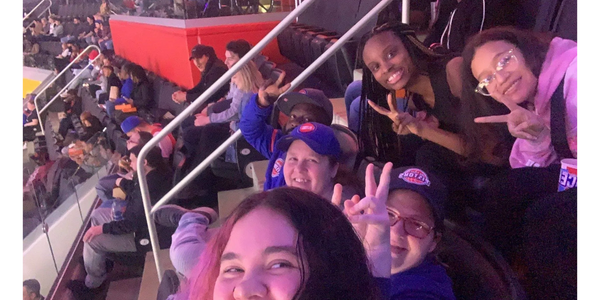 A group of people, sitting in rows of seats at a game. They are smiling and holding up peace signs.