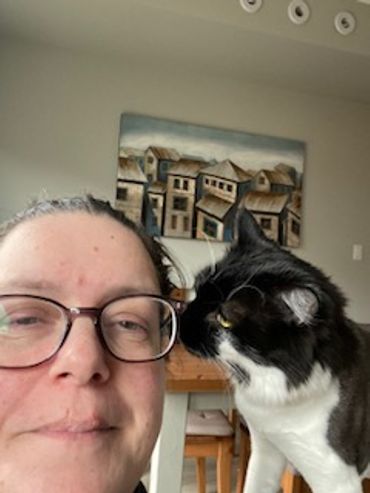 A woman with glasses and a black-and-white cat indoors.