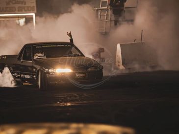 Black car drifting with smoke behind it at night.