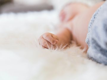 Blurred image of baby with Babys hand in forefront on soft blanket