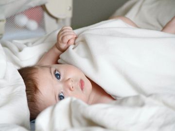Baby looking at camera while lying on a bed under blankets