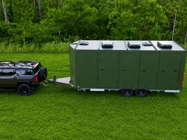 A black SUV towing a large green trailer on grass.