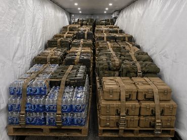 Stacks of bottled water and military cases secured with straps inside a storage container.