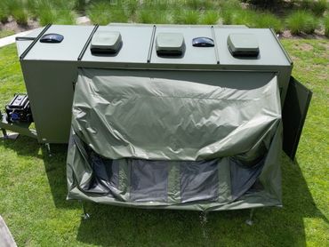 Military-style green trailer with canvas covering an extended section, parked on grass.
